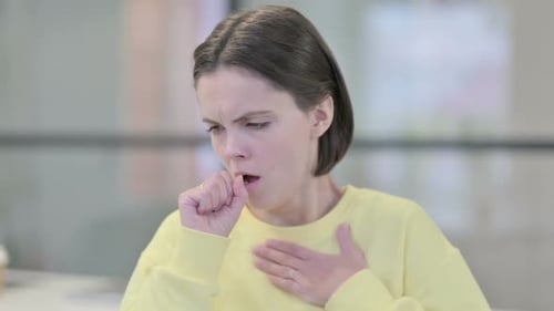 Young Woman Coughing into Her Fist Indoors