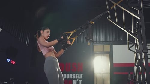 Asian young athlete sport woman using pull TRX rope exercise workout for health in fitness gym club.