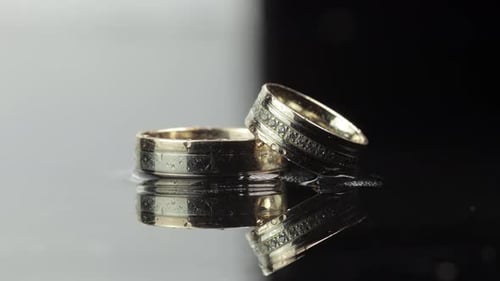 Wedding Rings on Black and White Water Surface Shining with Light. Close Up