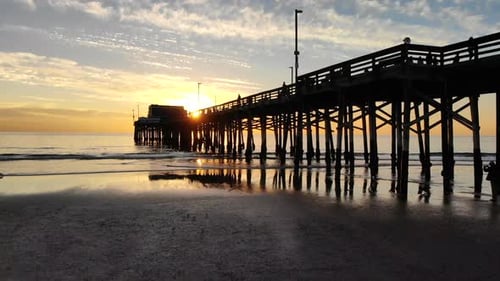 Drone shot at Newport Beach pier in California as sunlight beams through with sunset reflections on