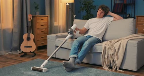 Un jeune garçon passe l'aspirateur compulsivement dans la chambre le soir alors qu'il est assis sur le canapé