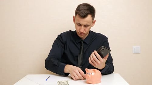 Serious Man Folds Dollar Bill and Inserts Into Piggy Bank
