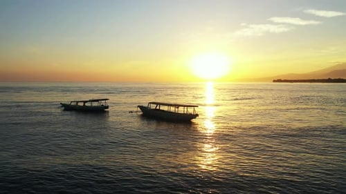Quiet paradise sunset with yellow sky reflecting over tranquil lagoon with silhouette of boats ancho