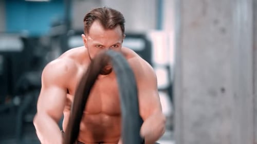 A Young Attractive Man Bodybuilder Battling Ropes with an Effort in the Sport Gym