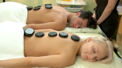 Beautiful Young Couple Enjoying Hot Stone Therapy in Spa Centre