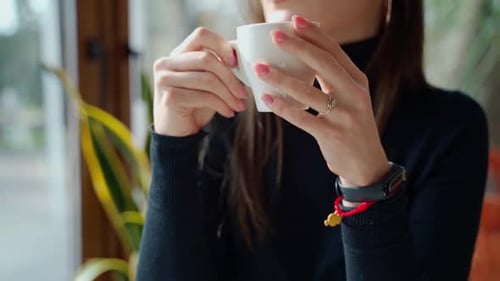 Beautiful girl drinking coffee in a cafe. Young woman sitting at the table near the window and enjoy