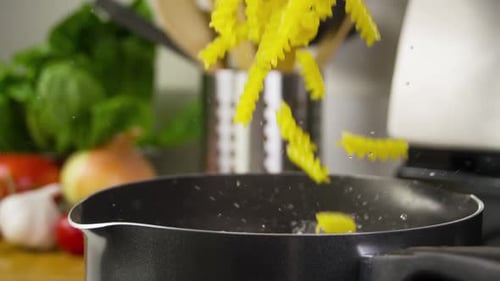 Yellow Pasta Falling into Boiling Water in Kitchen