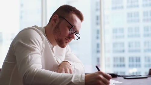Man Writing at Desk in Bright Office