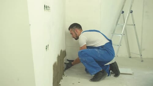 Builder Sits and Puts Tiles on the Wall