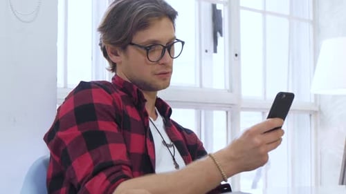 Close-up view of a man scrolling the feed in an app on his mobile phone in room