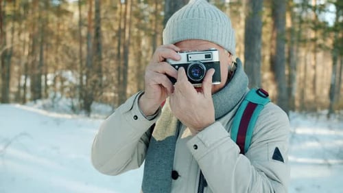 Retrato de homem sênior tirando fotos com câmera ao ar livre na floresta de inverno