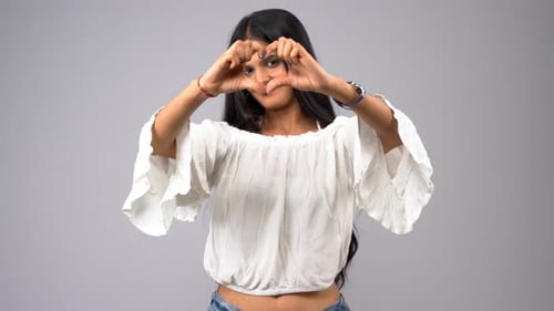 Woman Makes Heart Shape With Hands in Studio