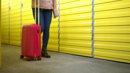 Jambes d'une jeune femme caucasienne méconnaissable marchant avec valise roulante le long d'une rangée de jaune