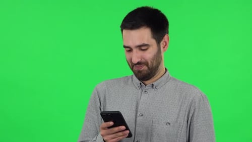 Porträt von Brunette Guy schreibt SMS auf seinem Handy und lächelt. Greenscreen