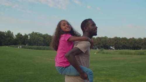 Happy Father Giving Daughter Piggyback Ride in Park