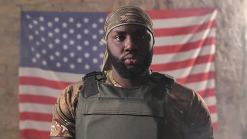 Man Wearing Military Gear in Front of Flag