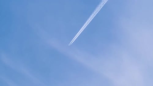 Distant Passenger Jet Plane Flying on High Altitude on Blue Sky with White Clouds Leaving Smoke