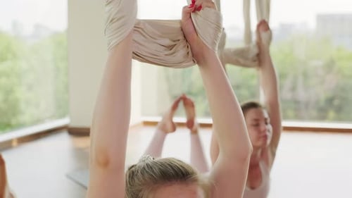 Young Adults Stretching with Aerial Yoga Straps Indoors