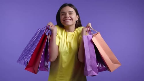 Excited Woman with Colorful Paper Bags After Shopping on Violet Studio Background