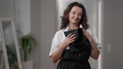 Mature Caucasian Woman Admiring Graduation Cap Standing at Home Indoors