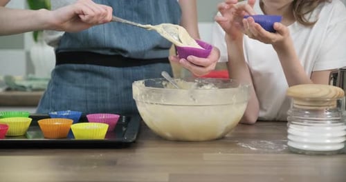 Nahaufnahme von Kinderhänden, die Teig in Cupcakes gießen