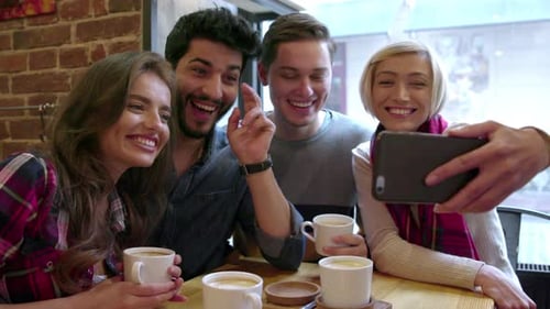 Happy friends making video call with mobile phone in cafe.