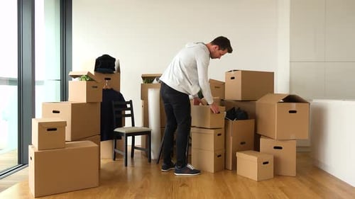 A Moving Man Replaces Cardboard Boxes From One Place To Another in an Empty Apartment