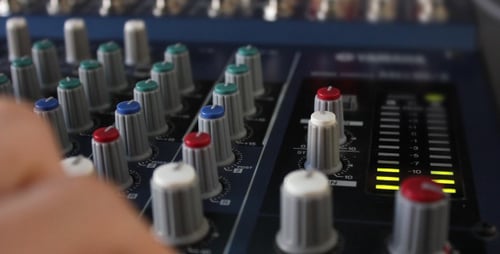 Hand Adjusting Levels on Audio Mixing Board