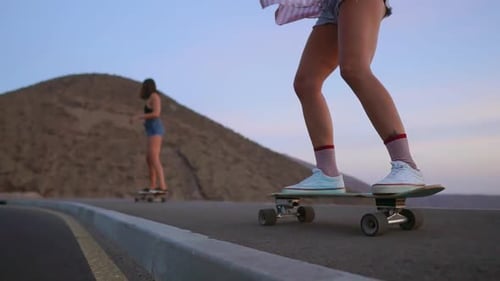 Two Girls Skateboarder Rides on a Board on the Slope Against the Sky From the Mountain. Slow Motion