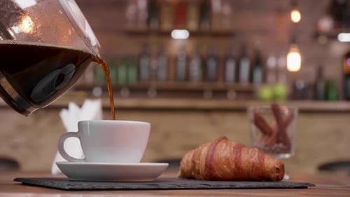 Close Up Shot of a Coffee Pot Filling a Cup To Serve with Croissant