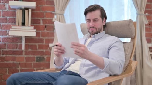 Man Examining Papers in Chair Indoors