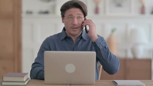 Young Man Talking on Phone while using Laptop in Office