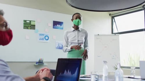 African american woman wearing face mask giving presentation to her colleagues at modern office