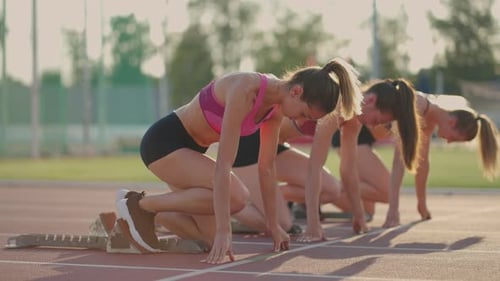 Three Young Women in the Stadium on the Start Line in Blocks Start in the Race in Slow Motion