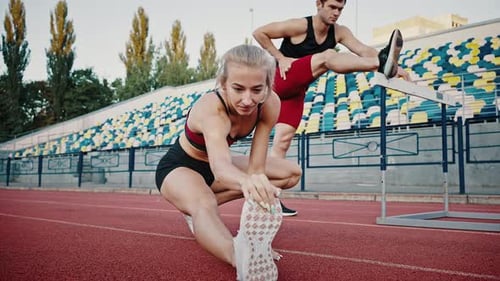 Primer plano de una chica y un chico estiran los músculos de sus piernas antes de un entrenamiento al aire libre