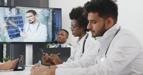 Equipo médico mestizo que escucha una presentación en Vídeo en una pizarra digital en la sala de oficina