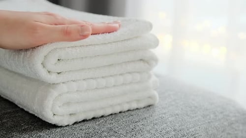 Hotel staff hands putting fresh white bath towels on the bed.