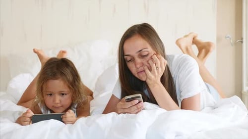Mother and Child Relaxing in Bed with Smartphones