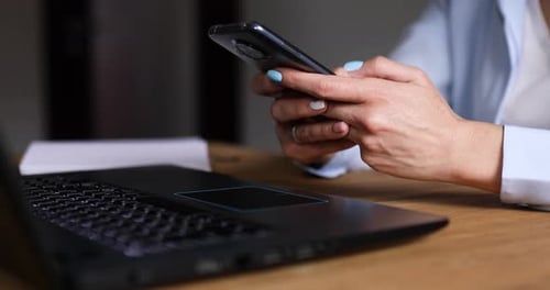Hands Using Phone Near Laptop on Wooden Desk