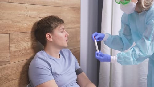 Health Professional in PPE Suit Introducing a Nasal and Throat Swab To Young Man Patient at Home