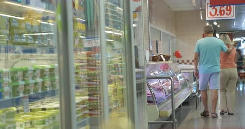 Couple Walking along the Fridges in Supermarket