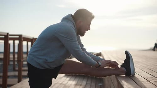 Man Stretches Leg on Boardwalk Near Ocean