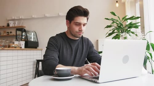 Young Hipster Businessman Working on Laptop in Cafe and Drinking Coffee