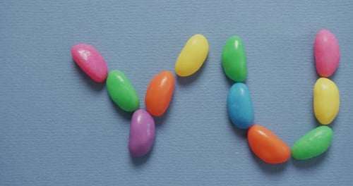 Video of overhead view of yummy text formed multi coloured sweets over blue background