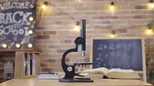 Sala de aula vazia com quadro-negro, microscópio de mesa e livro didático