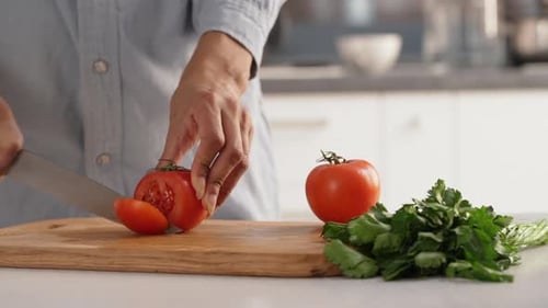 Gros plan montrant les mains d'une femme tranchant avec précision des tomates pour préparer une salade au ralenti