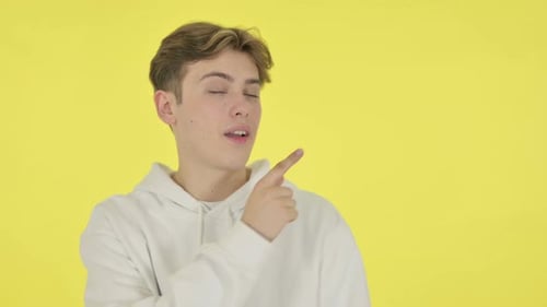 Young Man Points Right in Front of Yellow Backdrop