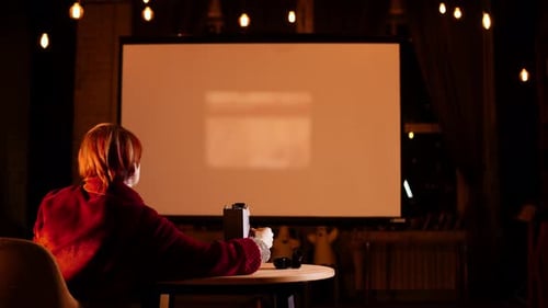 Una señora sentada en un sillón en una habitación acogedora inserta negativos fotográficos en el proyector de diapositivas para mostrarlos