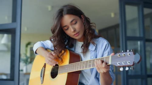 Woman Plays Guitar Smiling in Home Setting