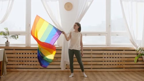 Young Adult Waves Rainbow Flag in Bright Room